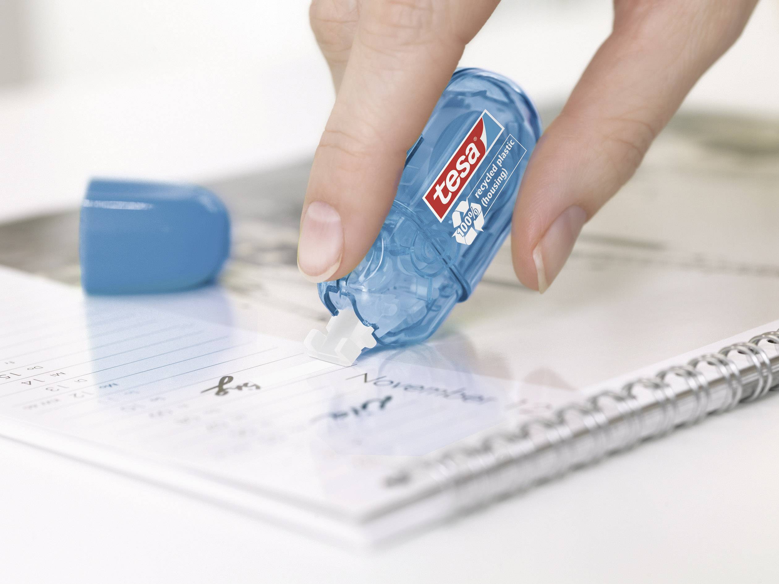 A hand is using a blue correction roller to correct errors on a notebook. The roller is branded 'tesa'.