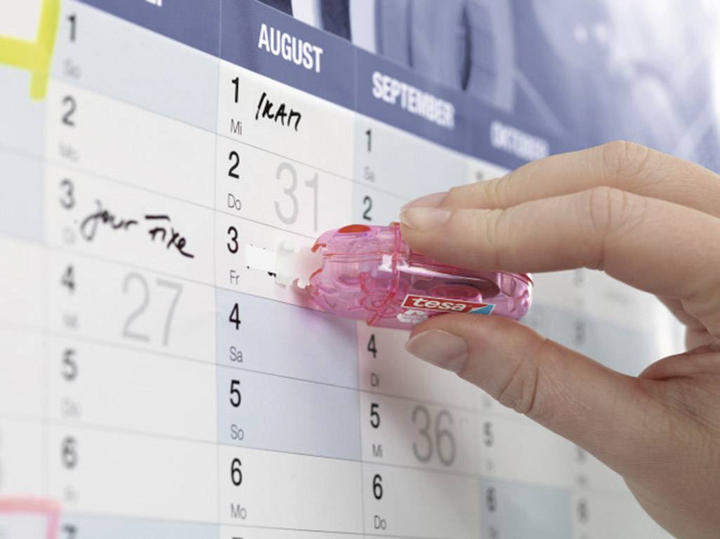 A hand uses a correction roller on a calendar to amend an entry. The month of August is in focus.