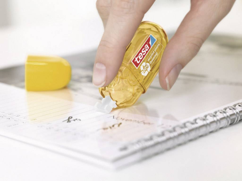 A hand uses a yellow Tesa correction roller to amend handwritten notes in a notebook.