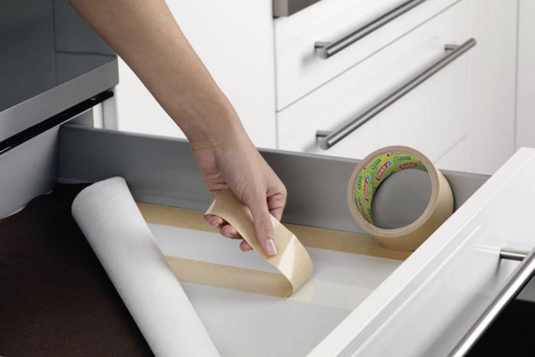 A hand places a piece of double-sided sticky tape into a drawer. Next to the hand lies a roll of tape.