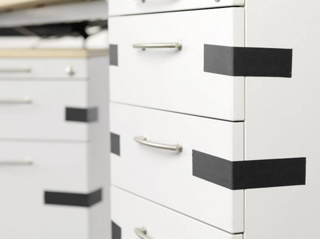 White filing cabinet with multiple drawers, sealed with black adhesive tape strips.