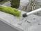 A net with green algae lies on a stone wall beside a pond. A rod with a black end can be seen next to it.