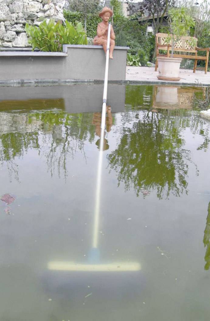 Person using a leaf net at the edge of a pond to remove leaves from the water. Garden furniture visible in the background.