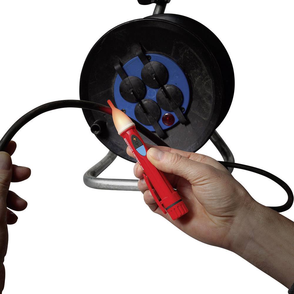 A person is testing a black cable from a cable drum with a red voltage tester to check for electrical current.