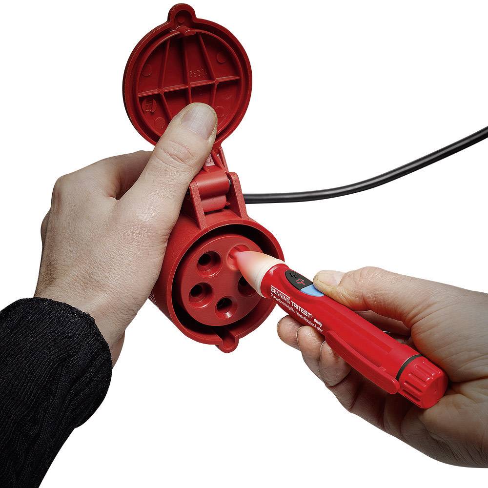 A person is holding a voltage tester against a red, round, three-pin electrical socket to check the voltage.