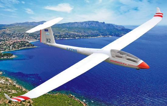 A glider soars over a coastal landscape with a blue sky and sea in the background, demonstrating elegance and expansiveness.
