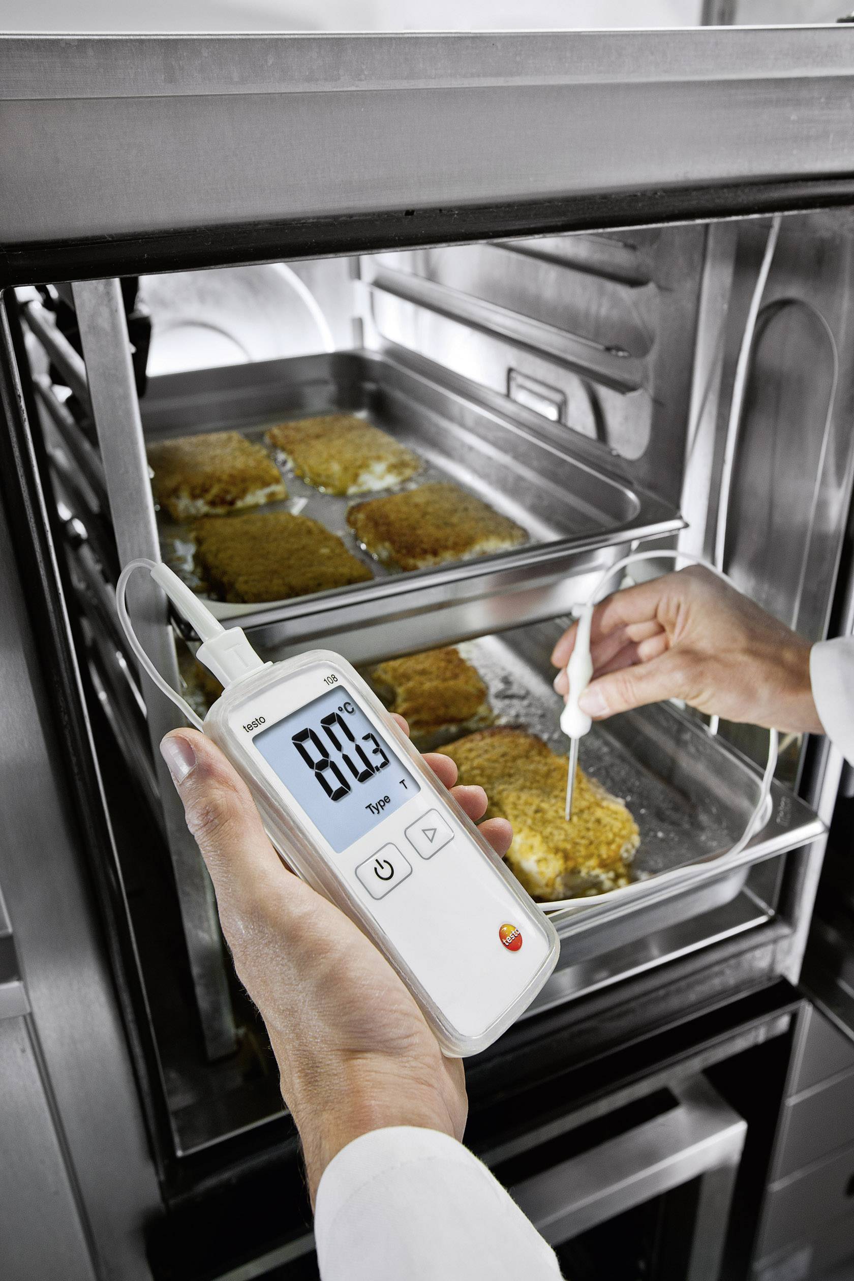 A person is measuring the core temperature of breaded schnitzels in an oven using a digital thermometer. The temperature shows 80.3°C.