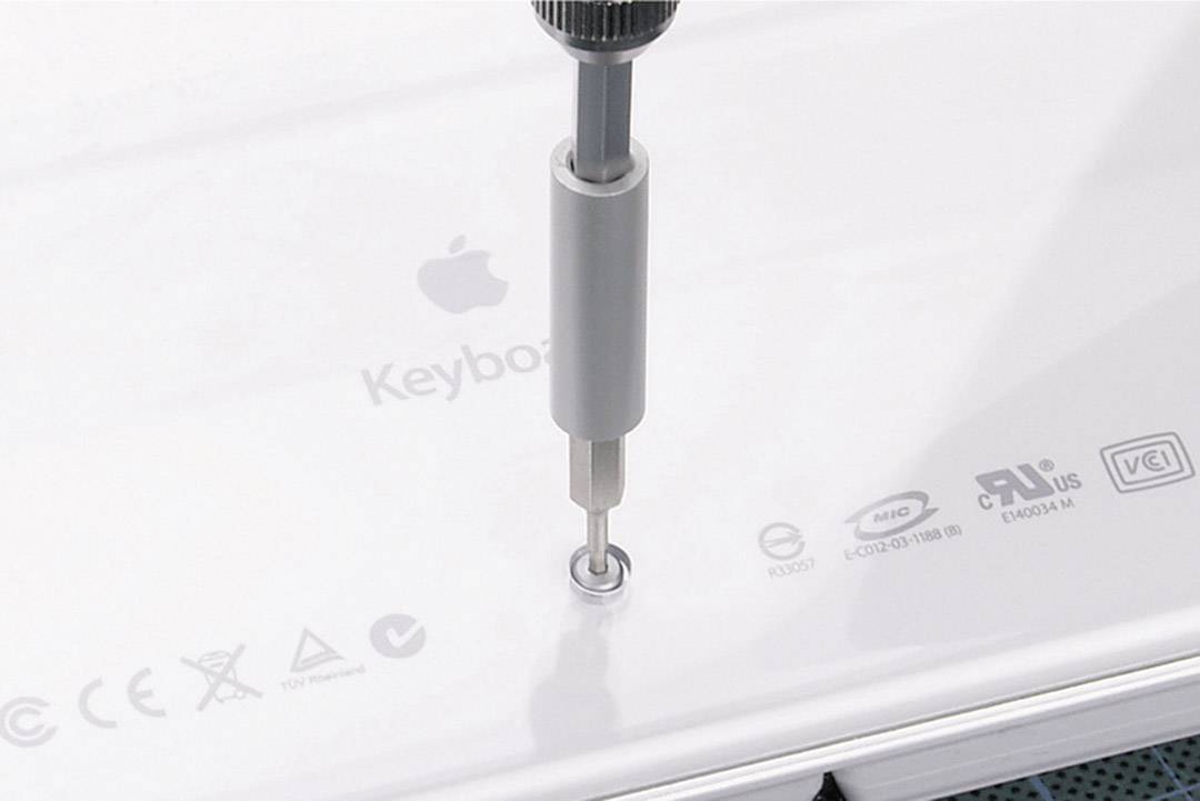 A screwdriver is securing a screw on a white device with visible symbols for safety and quality certifications.