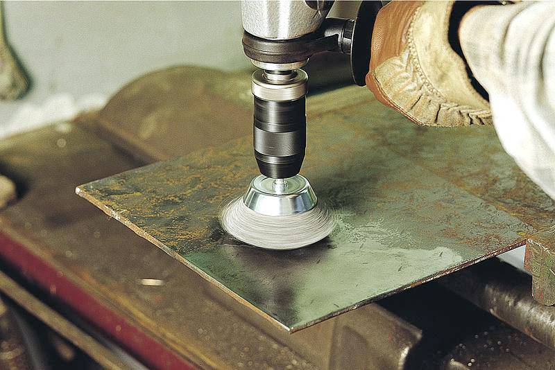 A hand holds an angle grinder working on a metal plate. The grinding machine throws up a shine on the plate.