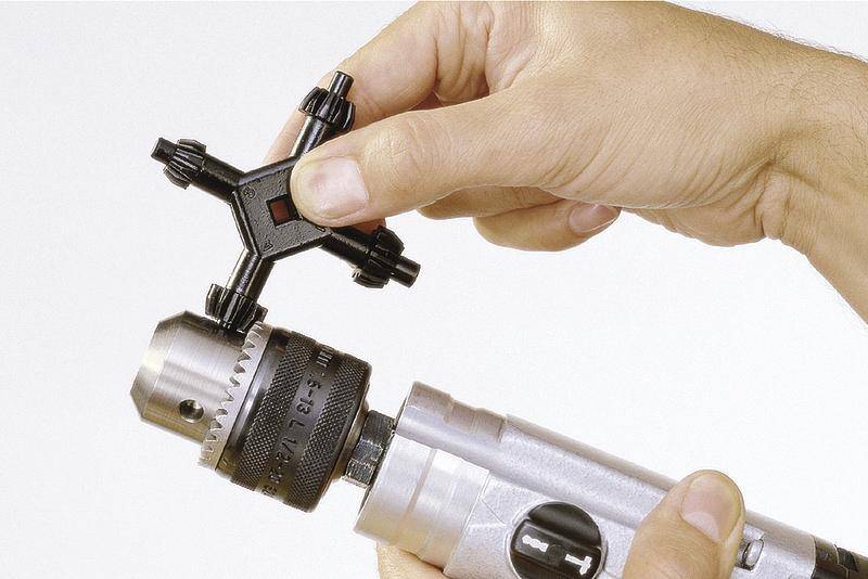 A person uses a chuck key to tighten or loosen the drill bit of a silver drill machine.