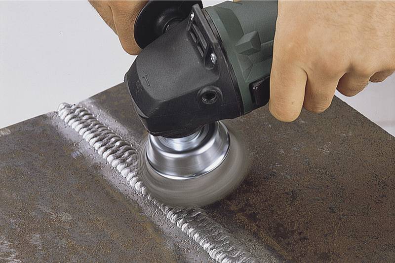 A person is grinding a weld seam on a metal plate using an angle grinder.