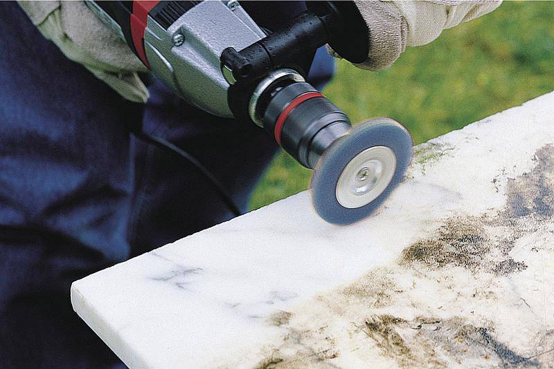 A person is polishing a white marble edge with a rotating tool. The surface shows the cleaning effect before and after.