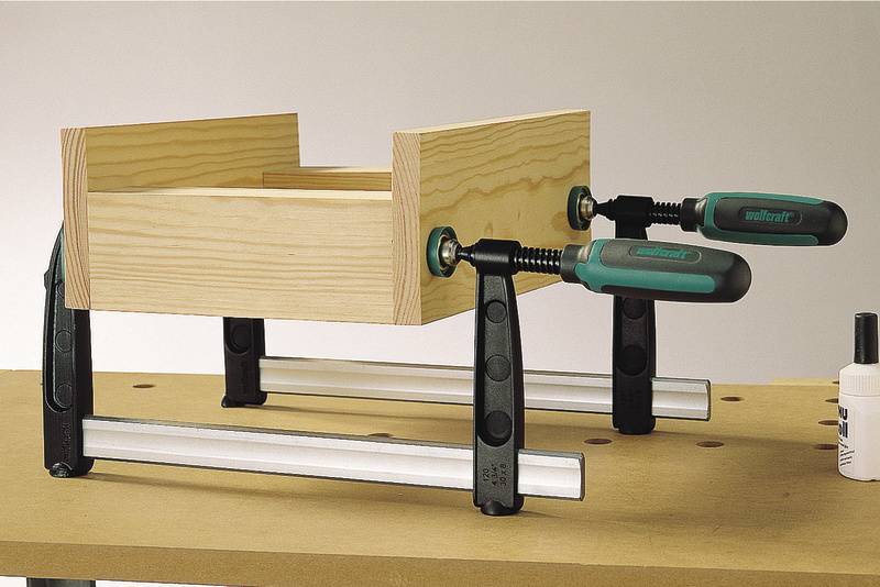 Wooden frame secured to a workbench using two G-clamps. The clamps have green handles.