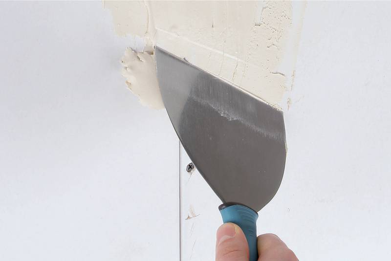 A hand holds a plastering trowel, applying white plaster to a wall. Wall repair in progress.