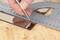 A hand is cutting glass with a glass cutter along a steel ruler resting on a wooden table.