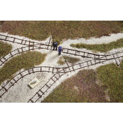 Two people are standing on a model railway layout with points and tracks, surrounded by grassy areas. A cardboard box is nearby.