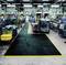 Large industrial hall with rows of machinery and a marked walkway made of non-slip material, protected by yellow markings.