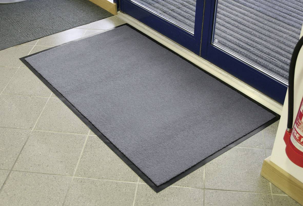 Grey doormat in front of a door on light tiles, prevents dirt in the entrance area. A fire extinguisher stands to the right.