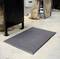 An anti-fatigue mat is lying on the floor next to a metal workstation in a workshop environment.