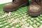 A pair of brown boots stand on a green grid mat, covered with wood chips.
