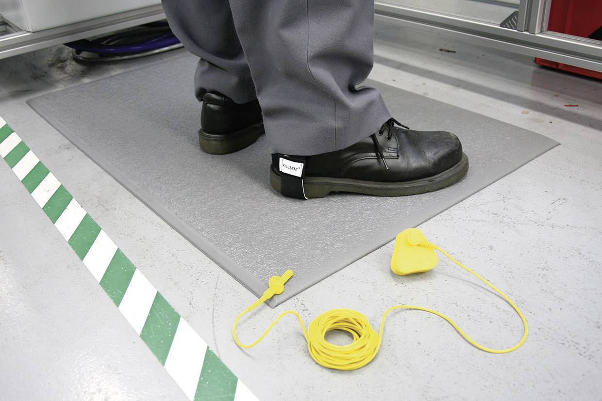 A person is standing on an anti-static mat, wearing black shoes. A yellow earthing strap is on the ground to prevent static discharge.