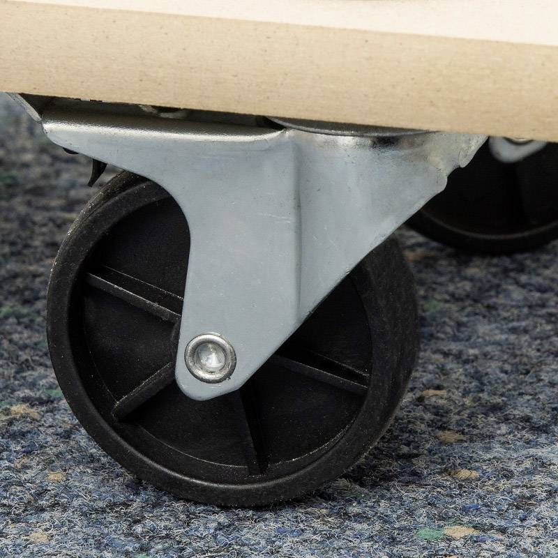 Close-up of a black, rotating wheel with a metal mounting, fixed to a wooden board, on a blue, patterned carpet floor.