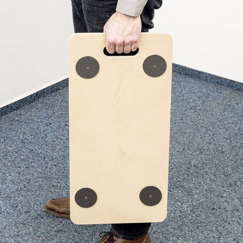 A person is holding a rectangular wooden board with four black round sliding surfaces on a blue carpet.