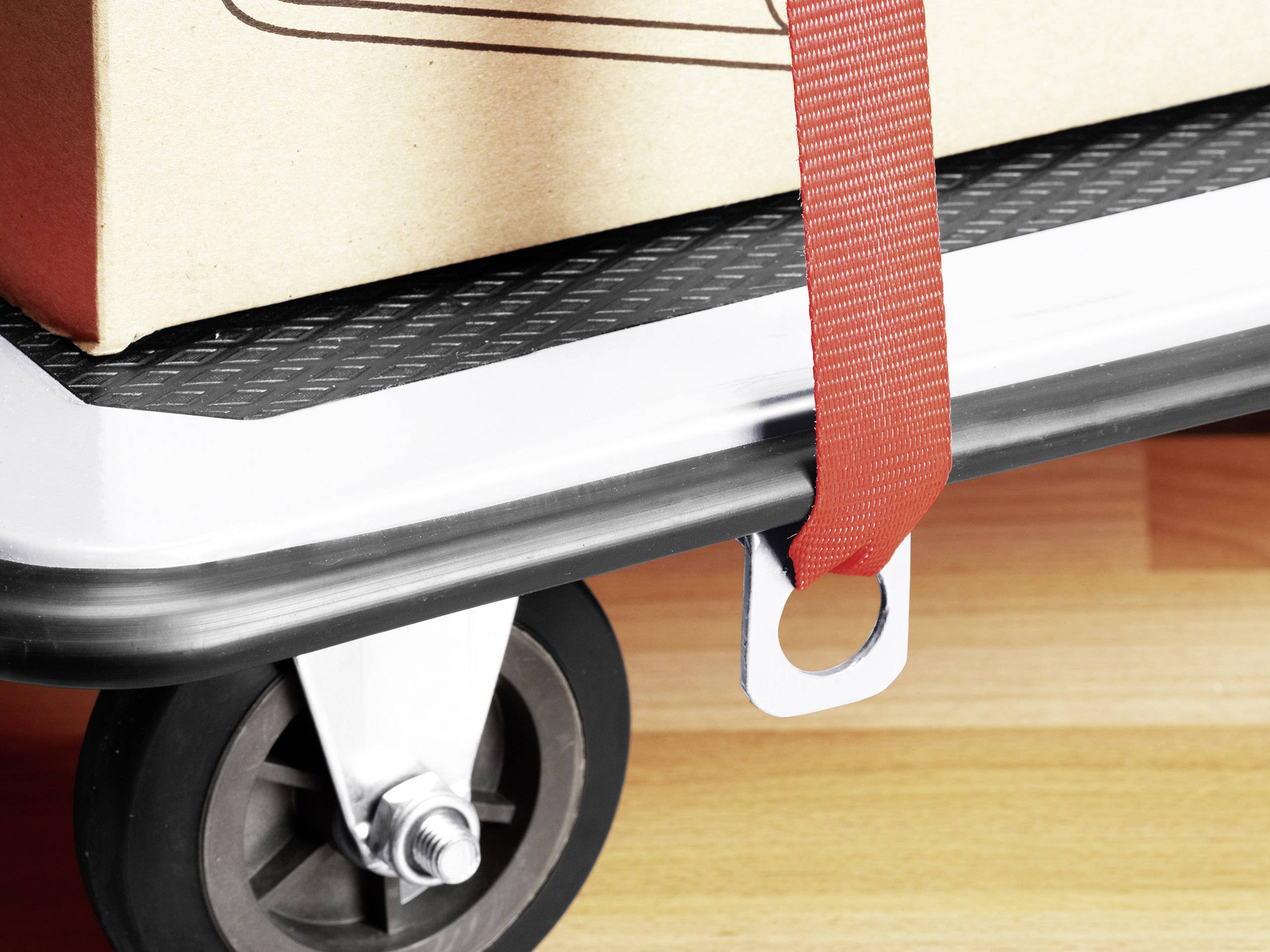 Close-up of a trolley with a crate on top, secured by a red strap.
