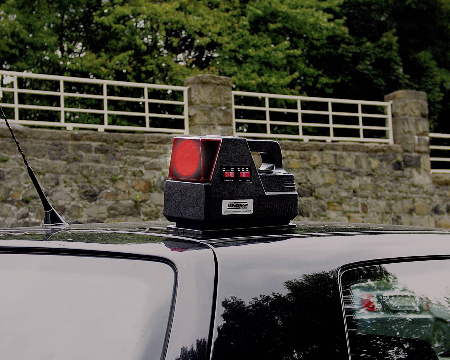 A mobile traffic monitoring device for speed measurement is mounted on a car roof. A stone wall is visible in the background.