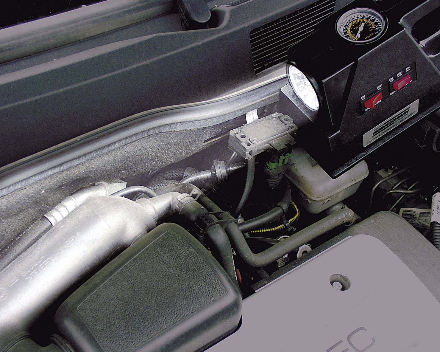 View of a vehicle's engine compartment with a diagnostic tool placed on the engine. Key engine components visible.