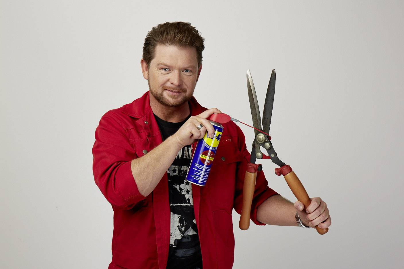 A man in red workwear is spraying lubricant onto a hedge trimmer.