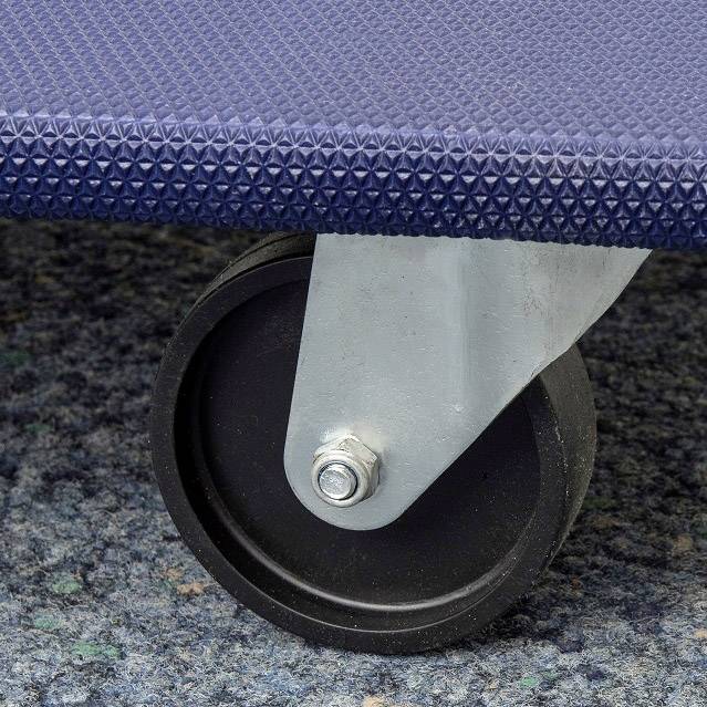 A black wheel of an office or industrial trolley with a blue surface in the background, on a patterned carpet.