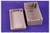 Grey plastic casing, two parts: lid and base, on a purple background. Rectangular shape with screw openings.