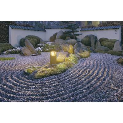 A illuminated stone garden at night with symmetrically raked gravel, rocks and plants, surrounded by a low white wall.
