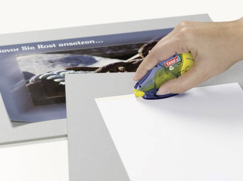 A hand is using a Sellotape roller to secure a white sheet of paper to a cardboard surface.