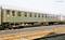 Green passenger train carriage stands on a railway track. Side row of windows. Field in the background.