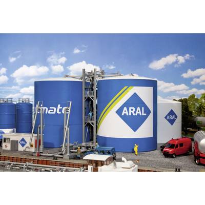 Large blue tanks with the 'ARAL' logo, surrounded by lorries and workers. Sky and trees in the background.