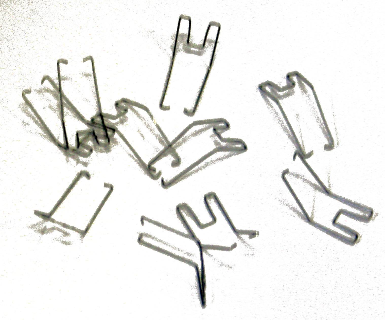 Metal cable clips scattered on a white surface. The clips are U-shaped and used for securing cables.