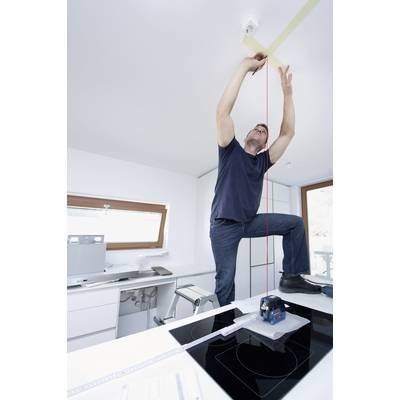 A person is installing a ceiling light in a modern kitchen. They are standing on a chair and holding a tape measure.
