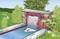 A brick well with a cascade of water falls into a rectangular pond, surrounded by green bushes and flowers.