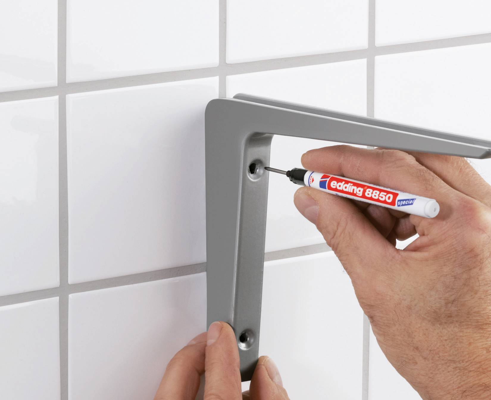 'A person is marking holes on a grey wall bracket on white tiles with a red pen.'