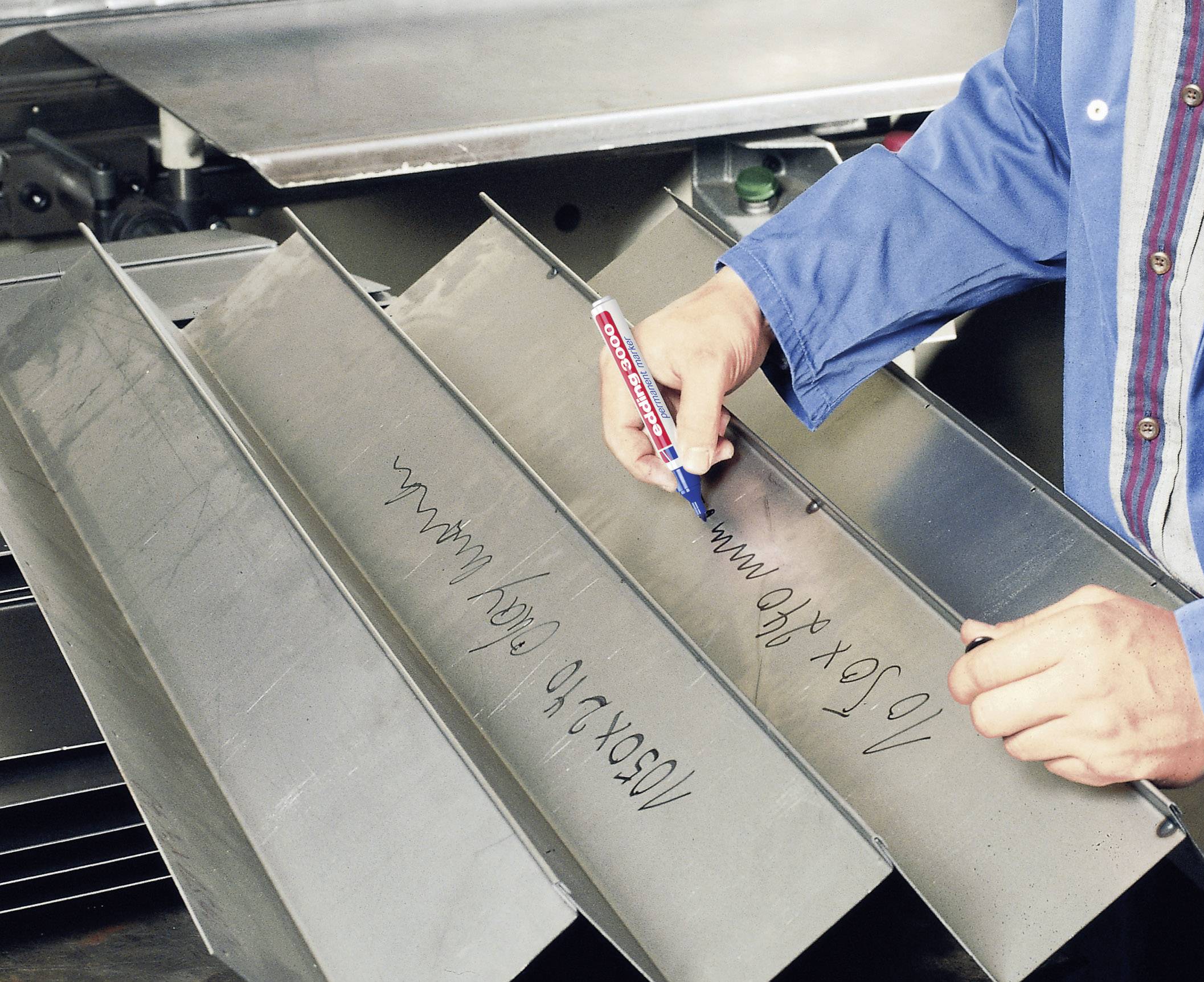 A person in a blue work jacket is writing mathematical formulas with a red pen on metal plates.
