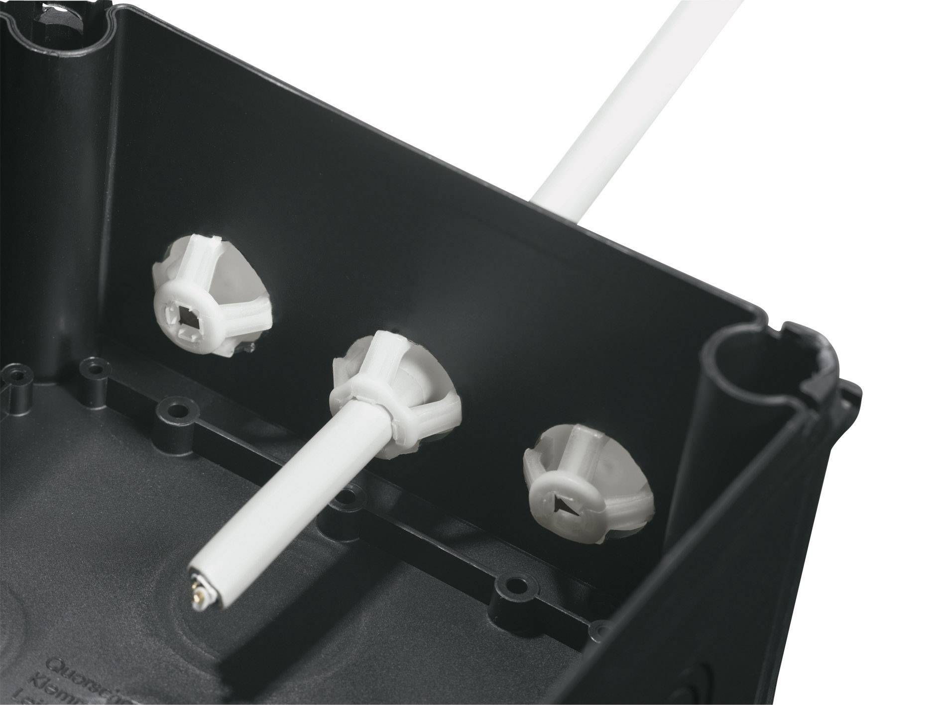 Close-up of a black enclosure with three white plastic fixings and a cable protruding from a mounting bracket.