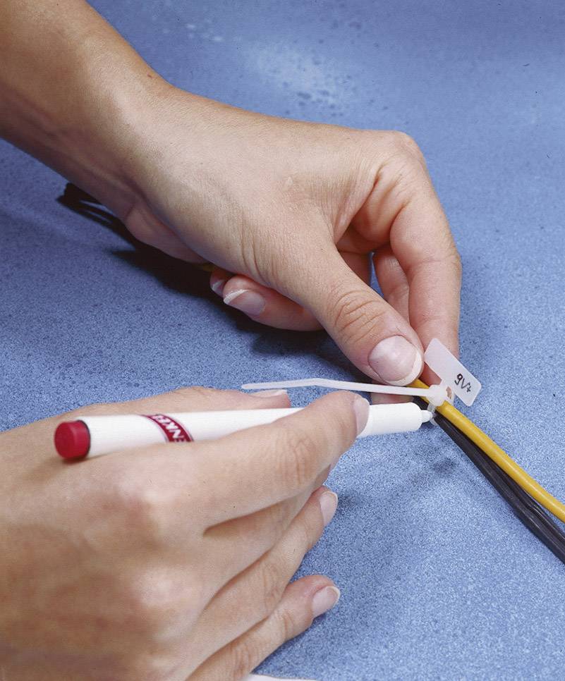 Two hands are labelling a cable with a white label and a red pen on a blue surface.