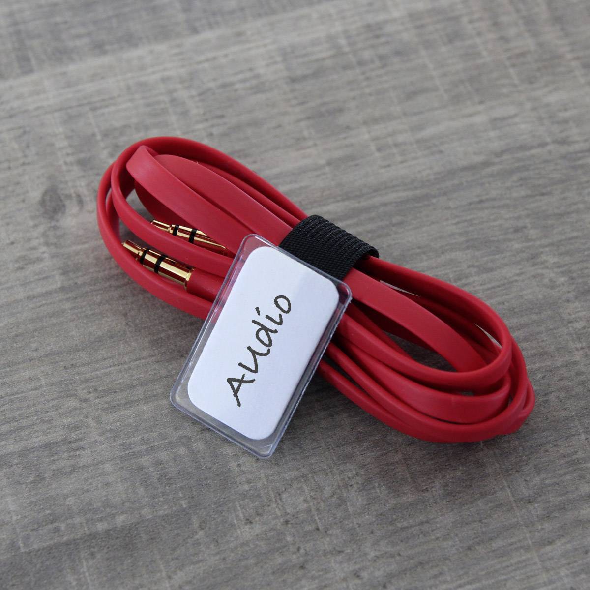 Red audio cable with gold-plated connectors, coiled up with a label marked 'Audio', lying on a wooden surface.