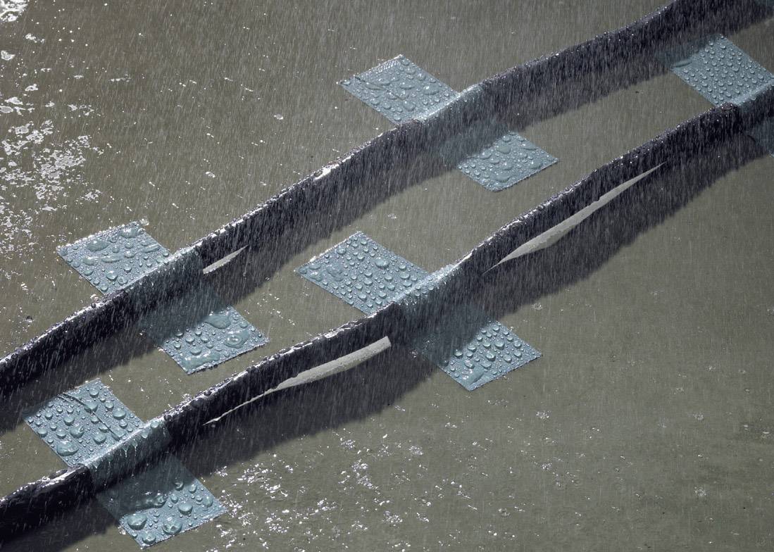 Rain falls on a swimming pool, with lanes separated by thick ropes. Blue marking pattern visible.