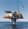 A large offshore drilling platform stands isolated in the sea, surrounded by clear sky and water, with cranes and working structures.