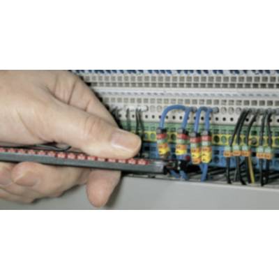 A hand holds a testing device and checks electrical connections in a control cabinet with wired connections.