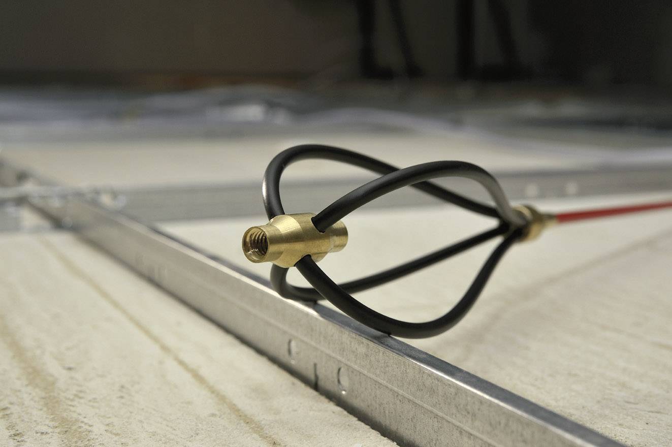 Close-up of a black cable routed through a metallic bracket on a concrete floor. The environment has an industrial feel.