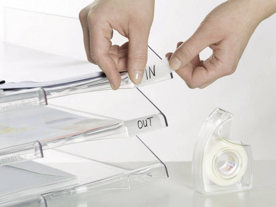 A person is placing documents into a three-part filing system with 'IN' and 'OUT' labels. A tape dispenser is situated beside it.